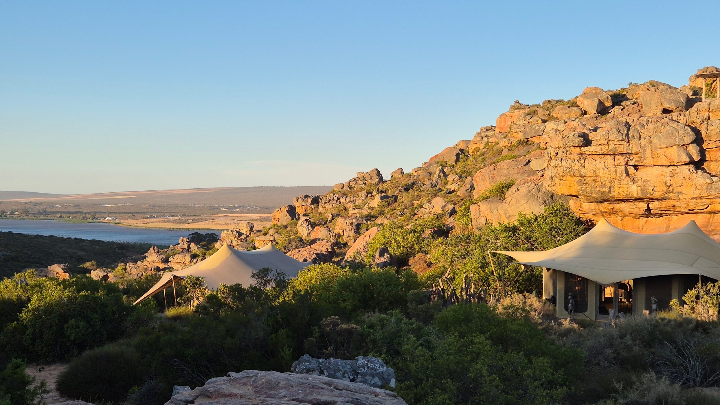 Tents among the sandstone rocks of Diepkloof under a blue sky, the valley beyond